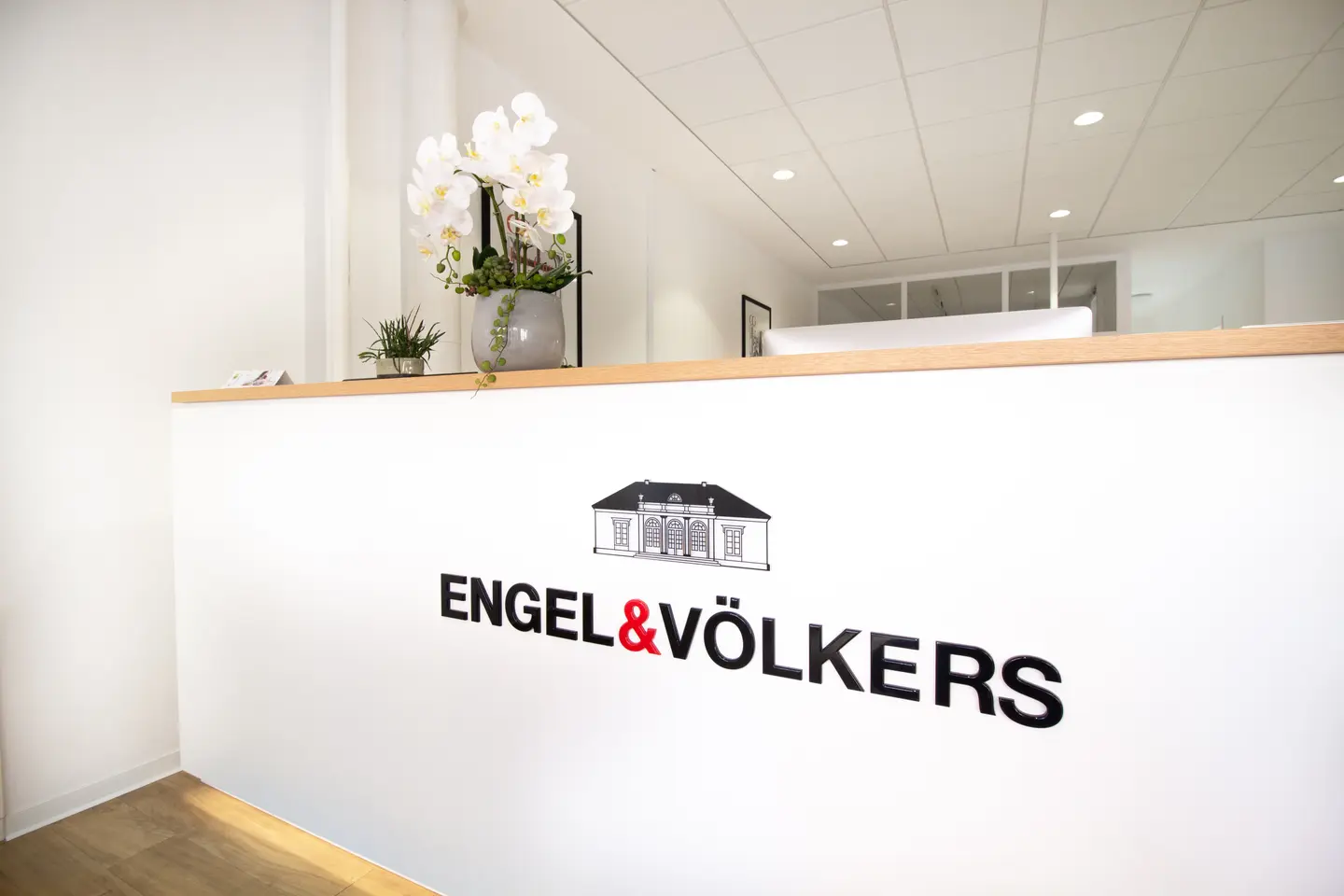 Engel & Völkers reception desk with logo, white orchids, and light wood trim.