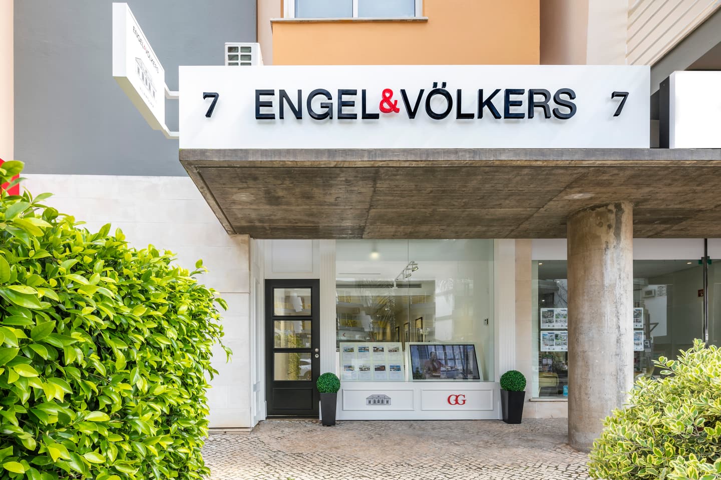 Engel & Völkers real estate office exterior with green bushes and a concrete awning.
