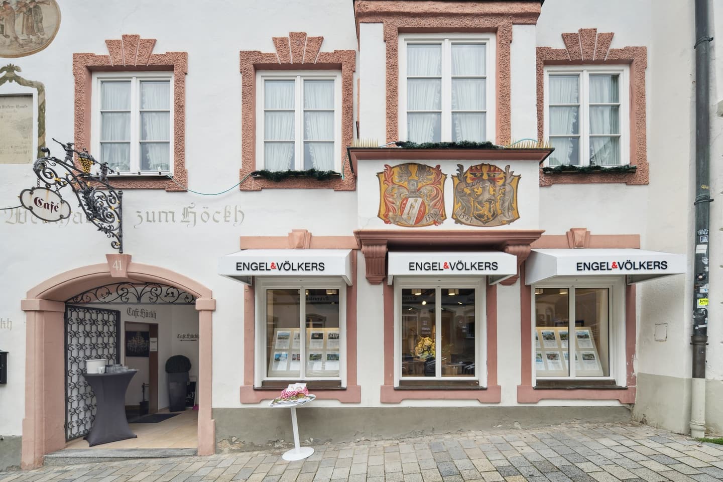 Engel & Völkers real estate office on a European street. The building is white with red trim and has large windows.