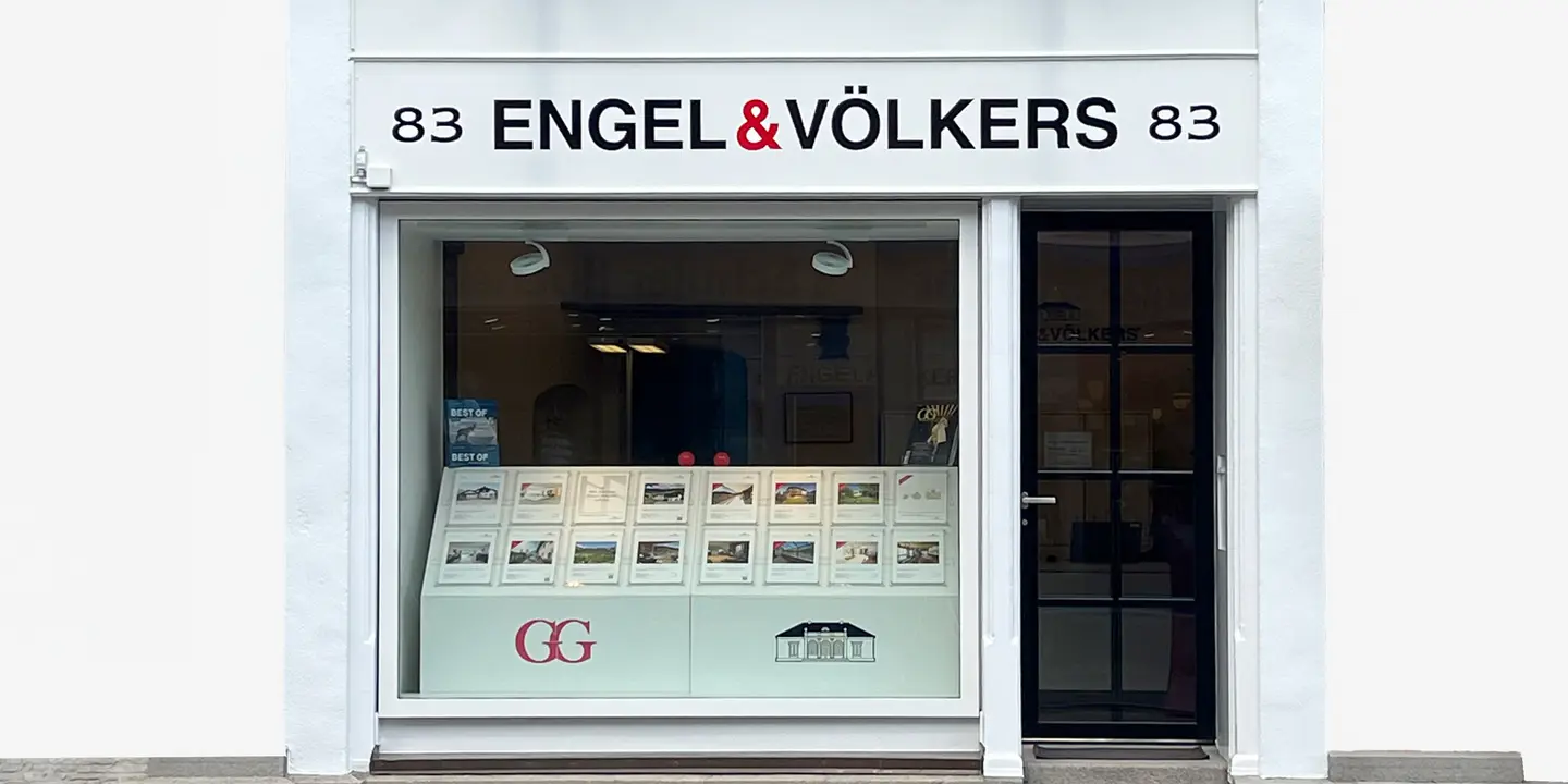 Engel & Völkers real estate storefront with a black door and window display of property listings.