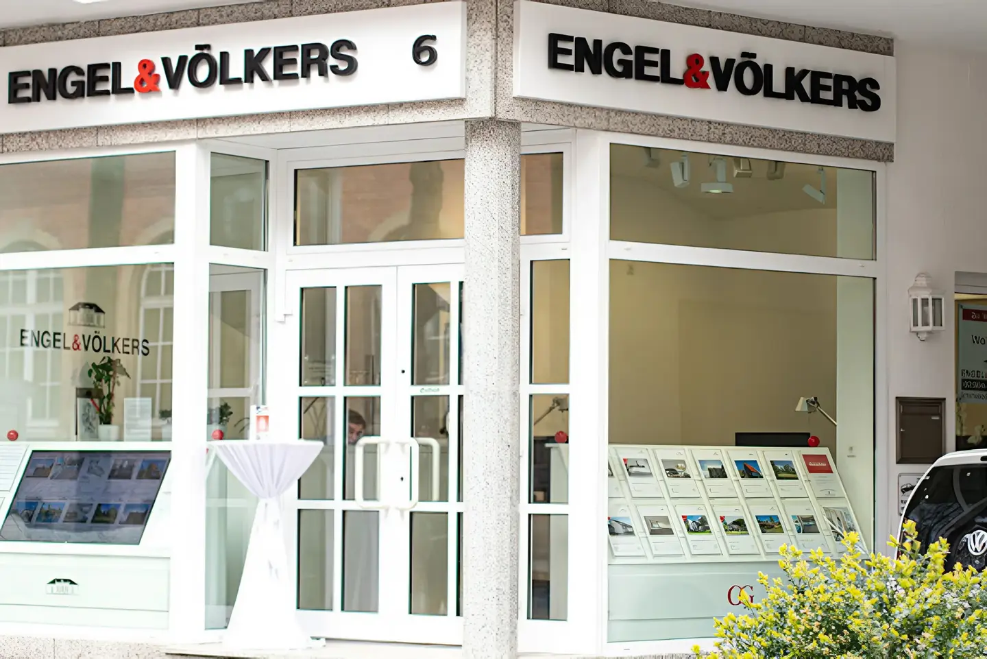 Engel & Völkers real estate office exterior with white trim, glass windows, and property displays.