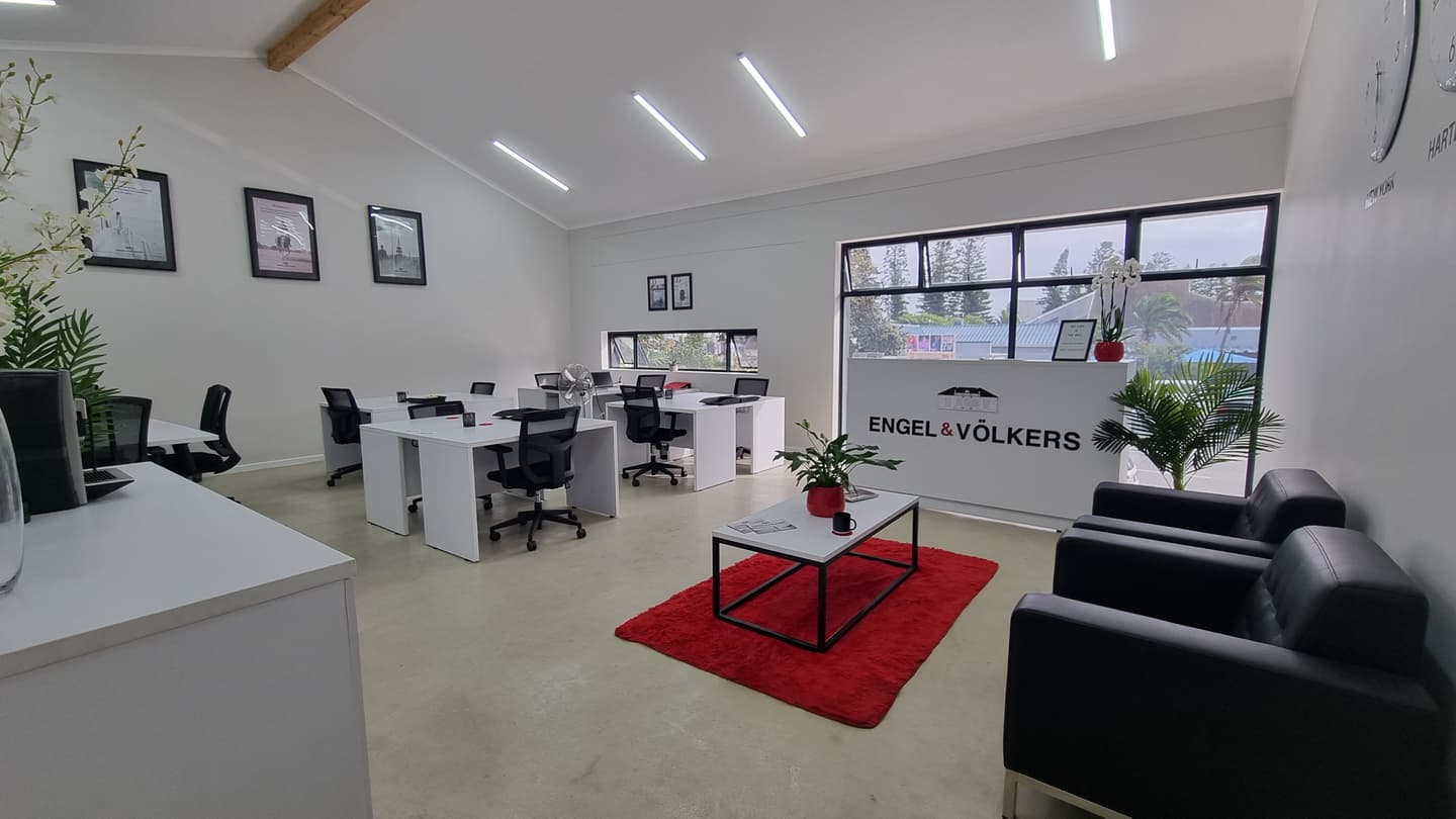 Engel & Völkers office interior with white desks, black chairs, and a red rug. The reception area has black leather chairs.