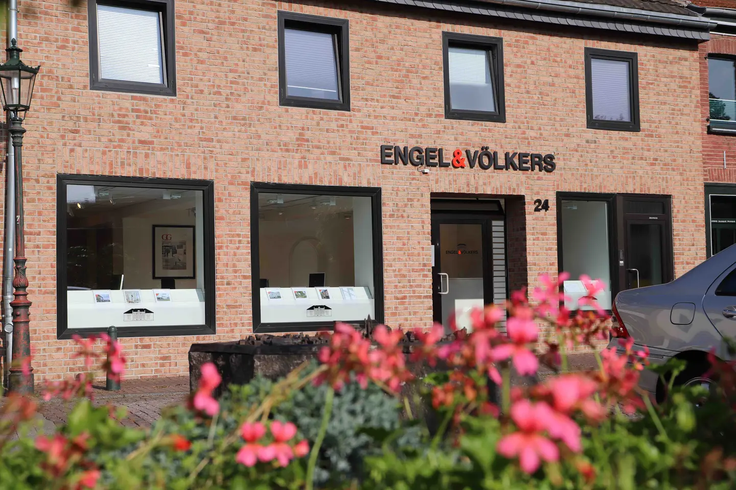 Engel & Völkers real estate office with brick facade, black window frames, and pink flowers in the foreground.