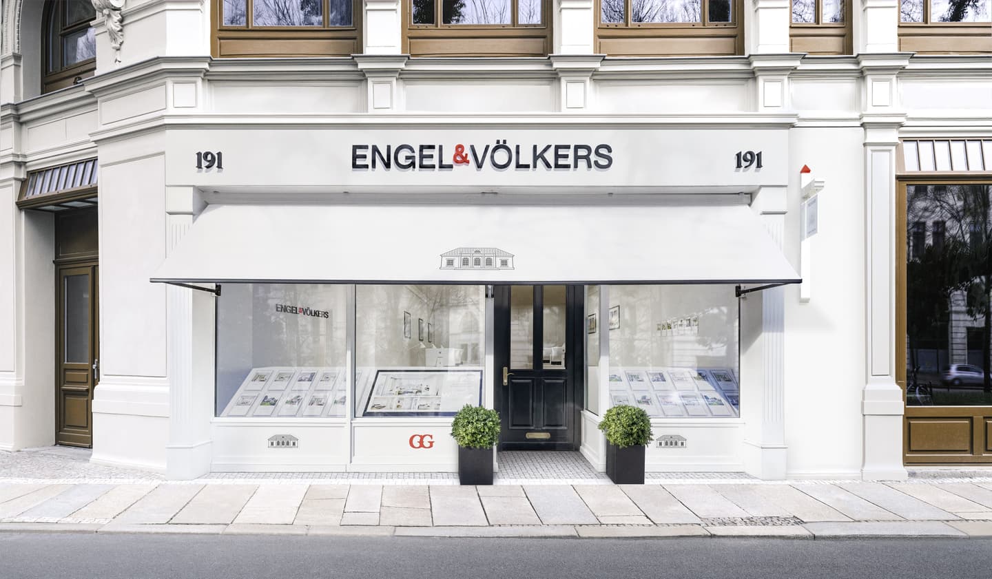 Engel & Völkers real estate office front with white awning, black door, and property listings in the window.