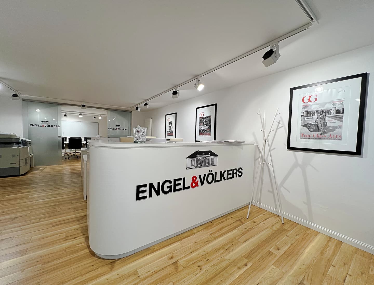 Engel & Völkers real estate office with a white reception desk, black logo, and a black leather sofa.