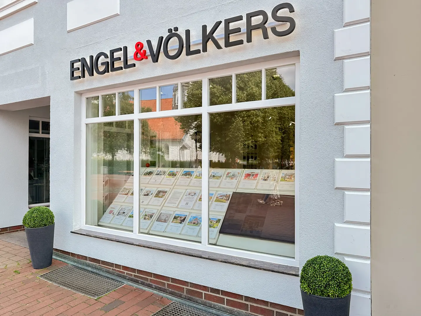 Engel & Völkers real estate office with a large window displaying property listings. The building is white with black lettering.