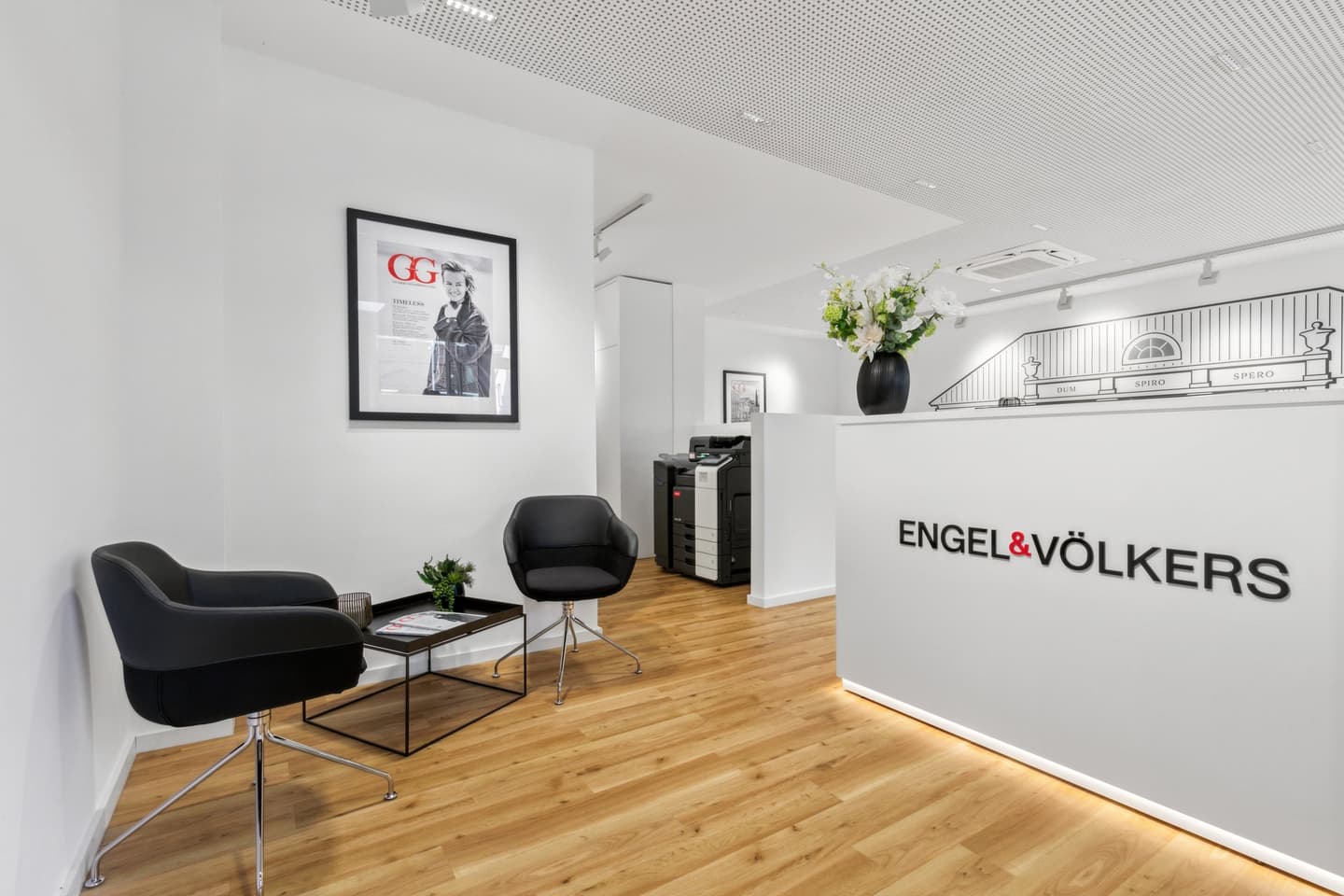 Außenansicht des Engel & Völkers Immobilienbüros mit großen Fenstern, in denen Immobilienangebote und ein digitaler Bildschirm zu sehen sind.