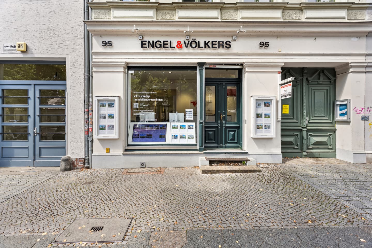 Engel & Völkers real estate office front with dark green door and window displays, on a cobblestone street.