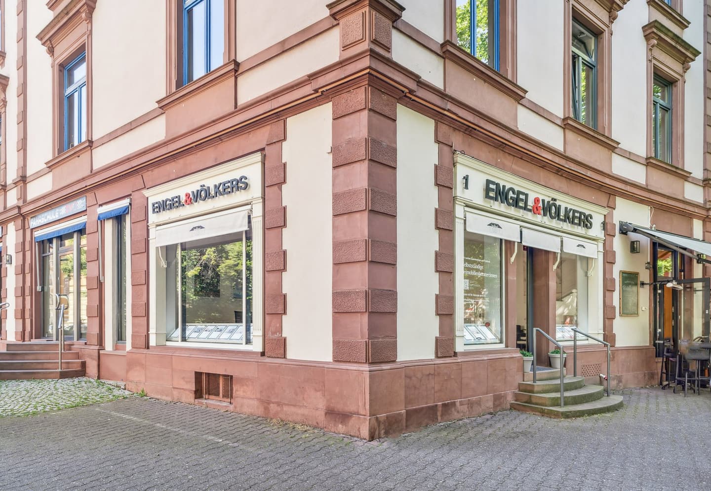 Engel & Völkers Immobilienbüro, Außenansicht. Glasfenster zeigen Immobilienangebote. Stufen führen zum Eingang.