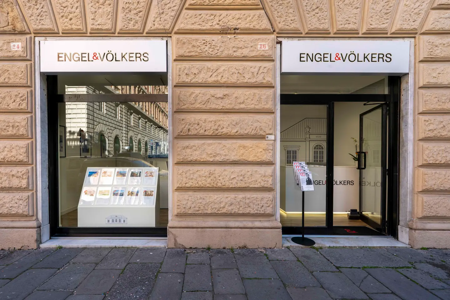 Engel & Völkers real estate office with stone facade. A window displays property listings, and the door is open.