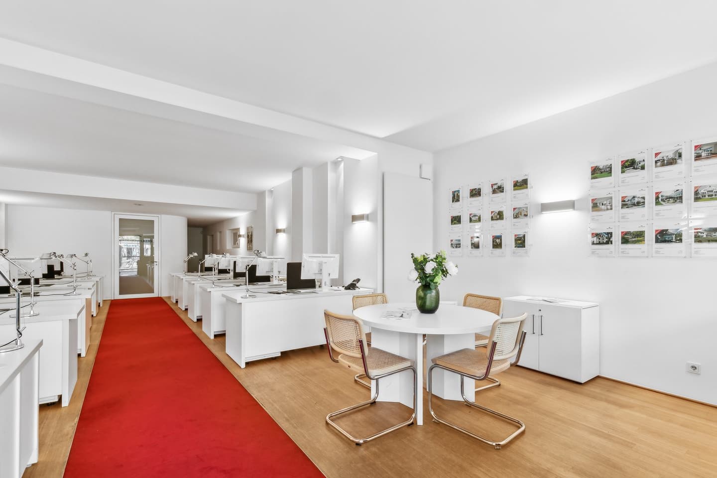 Engel & Völkers Immobilienbüro-Schaufenster. Weißes Gebäude mit schwarzer Tür, Markisen und Immobilienangeboten in den Fenstern.