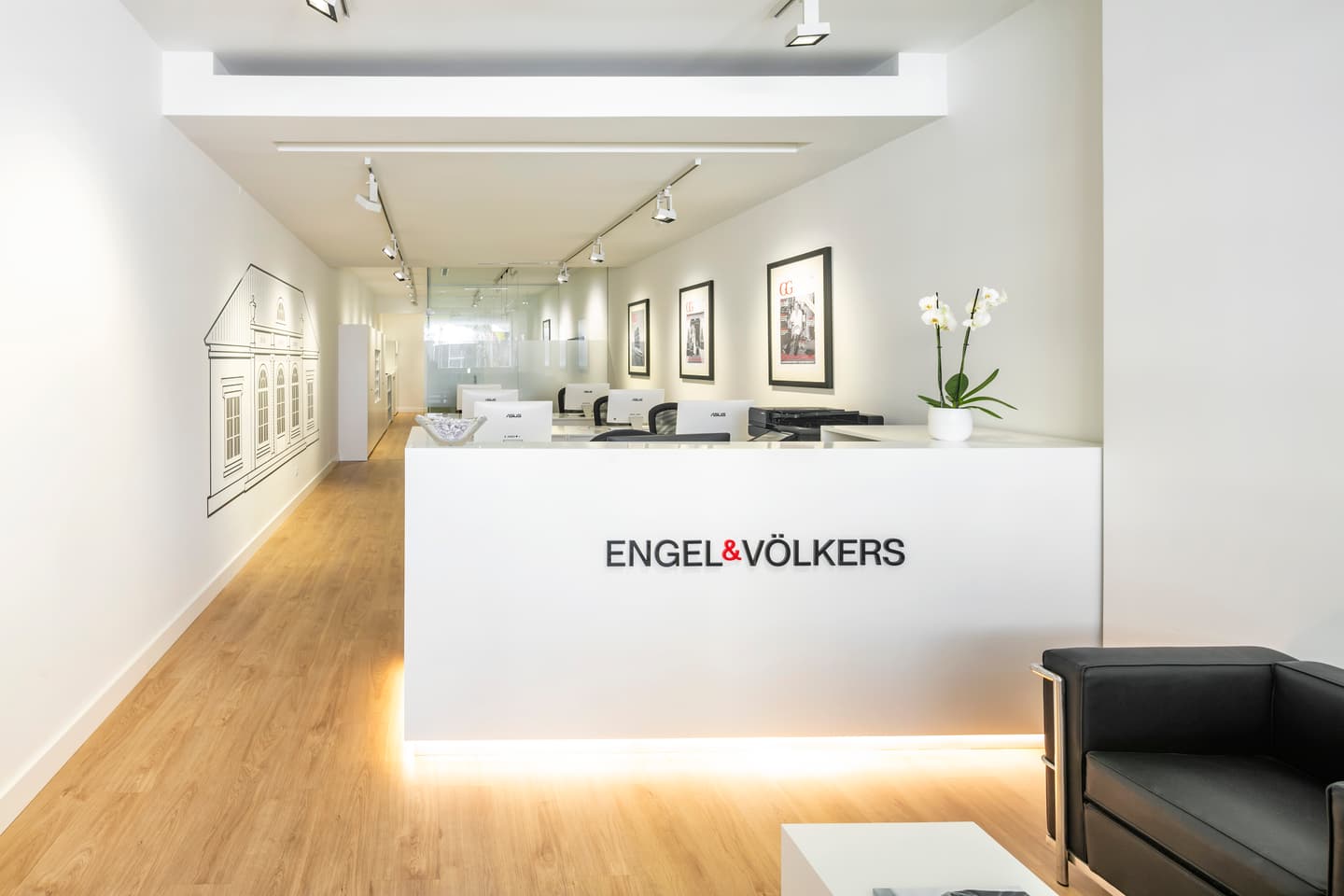 Engel & Völkers real estate office with a white reception desk, wood floors, and black leather chair.