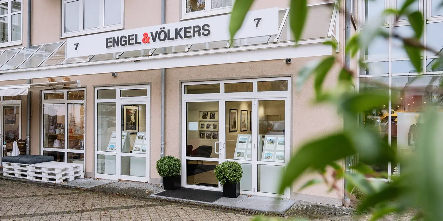 Exterior of Engel & Völkers real estate office with white framed windows and doors. Signage above reads "Engel & Völkers" and "7".