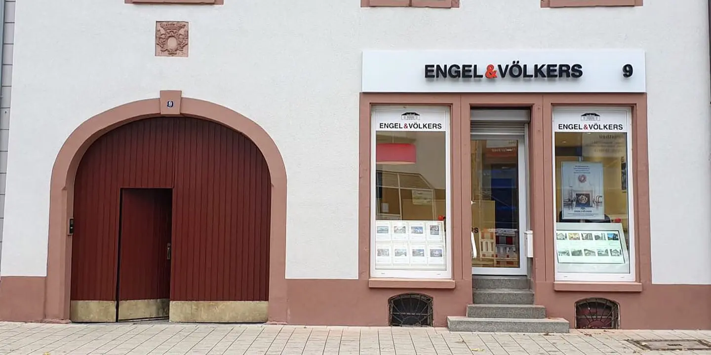Engel & Völkers real estate office with a large arched wooden door and window displays. The building is white with brown trim.