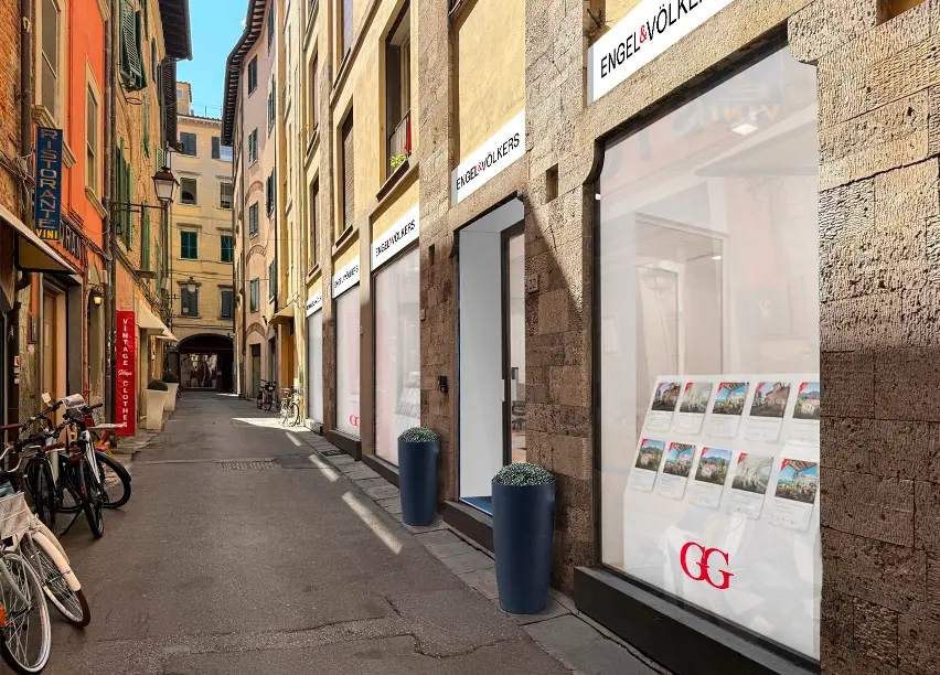 Engel & Völkers Geschäft auf einer schmalen Straße in Italien, mit Fahrrädern in der Nähe geparkt.