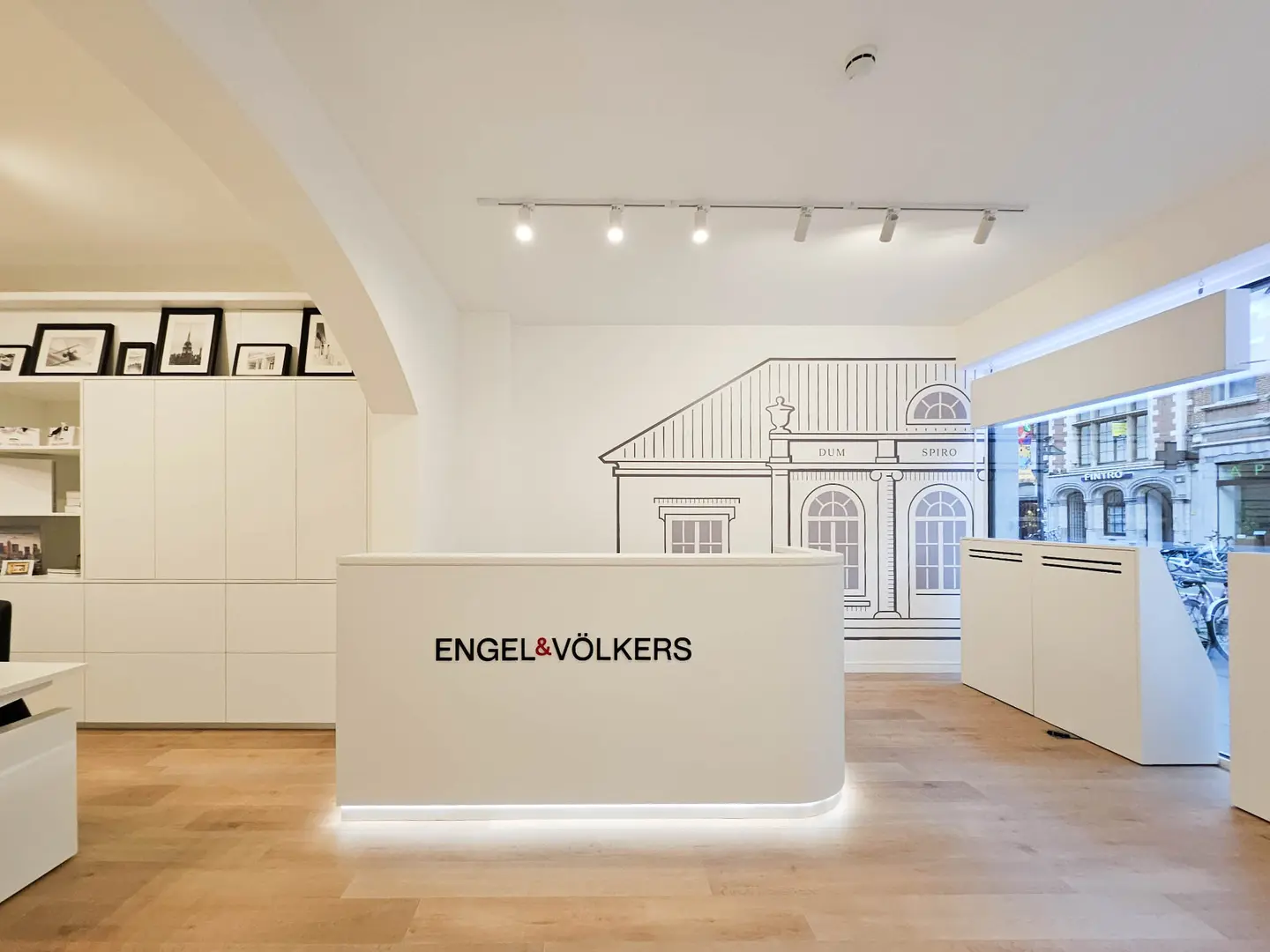 Intérieur du bureau Engel & Völkers avec une réception blanche, des planchers en bois et une murale d'un bâtiment.