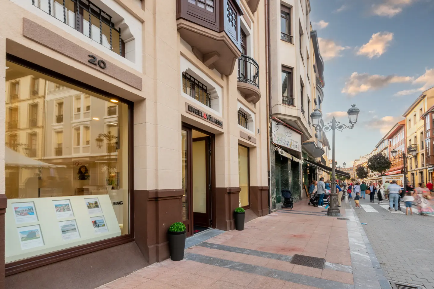Oficina immobiliària d'Engel & Völkers en un carrer concorregut de la ciutat. L'edifici és beix amb detalls marrons i grans finestrals. Hi ha gent que camina per la vorera.