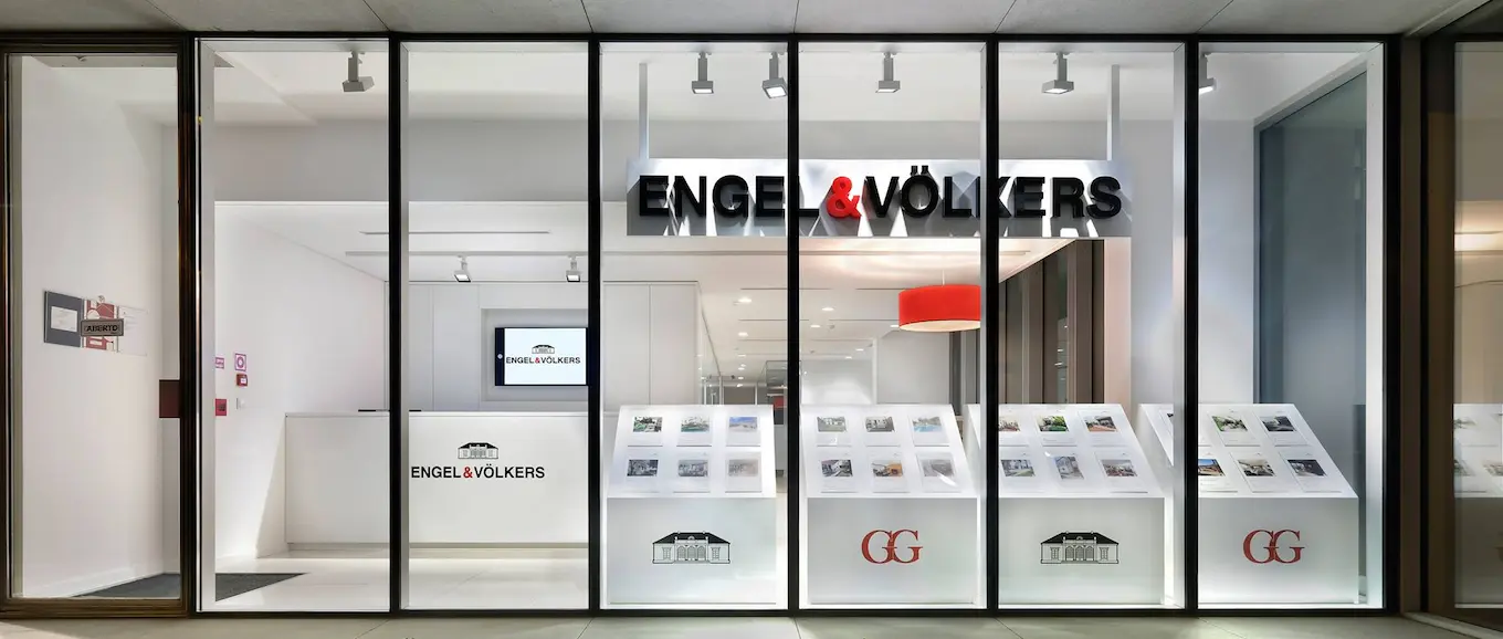 Engel & Völkers real estate office storefront with black framed glass windows and white interior.