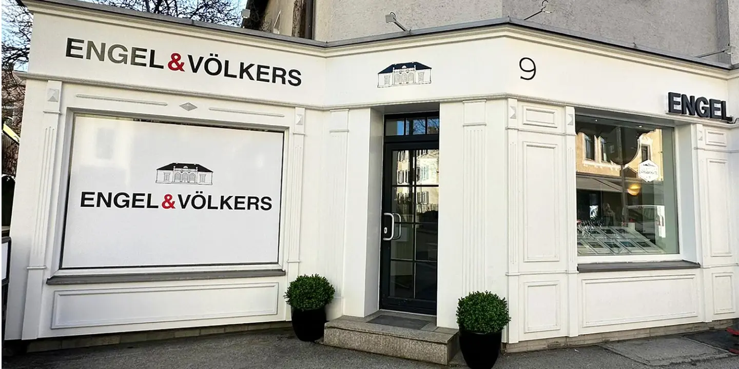 Engel & Völkers real estate office exterior. White building with black lettering and door. Number 9 above the door.