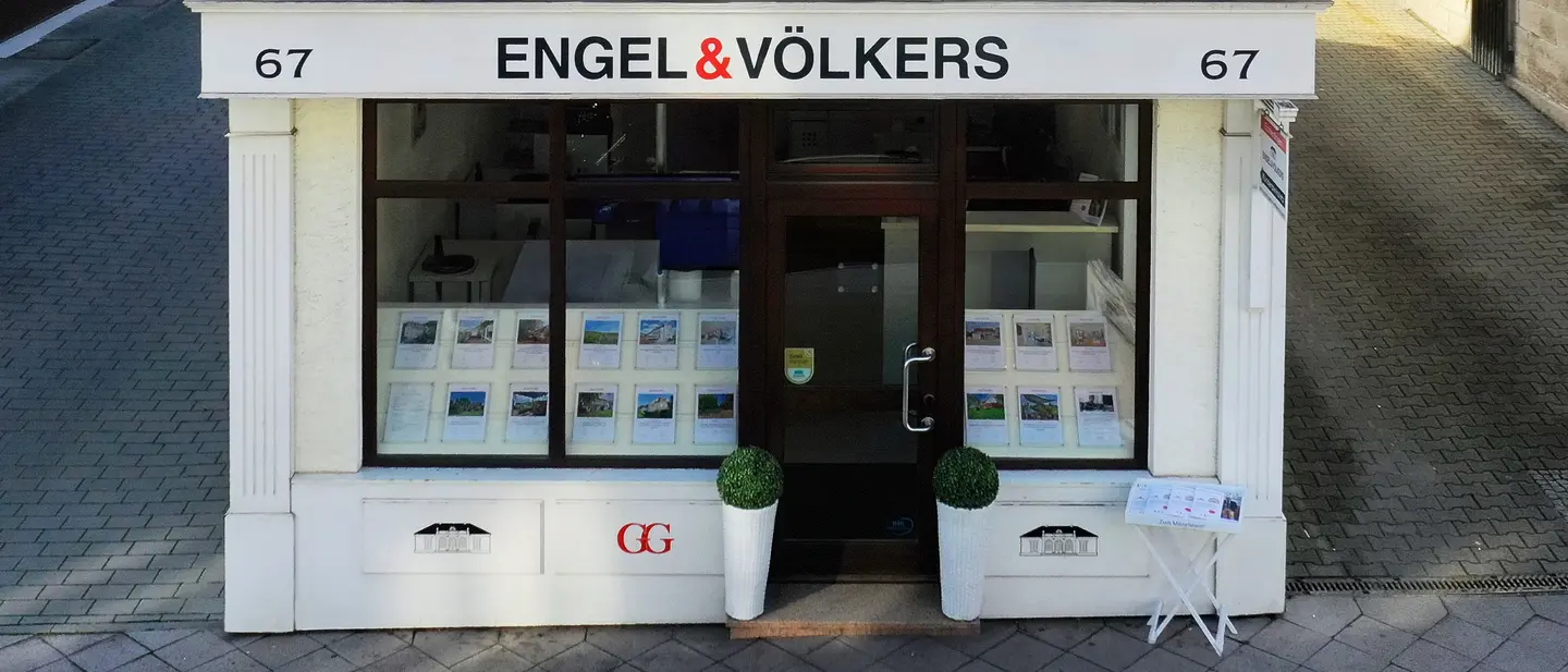 Engel & Völkers real estate office with a white facade, brown door and window frames, and property listings displayed in the window.