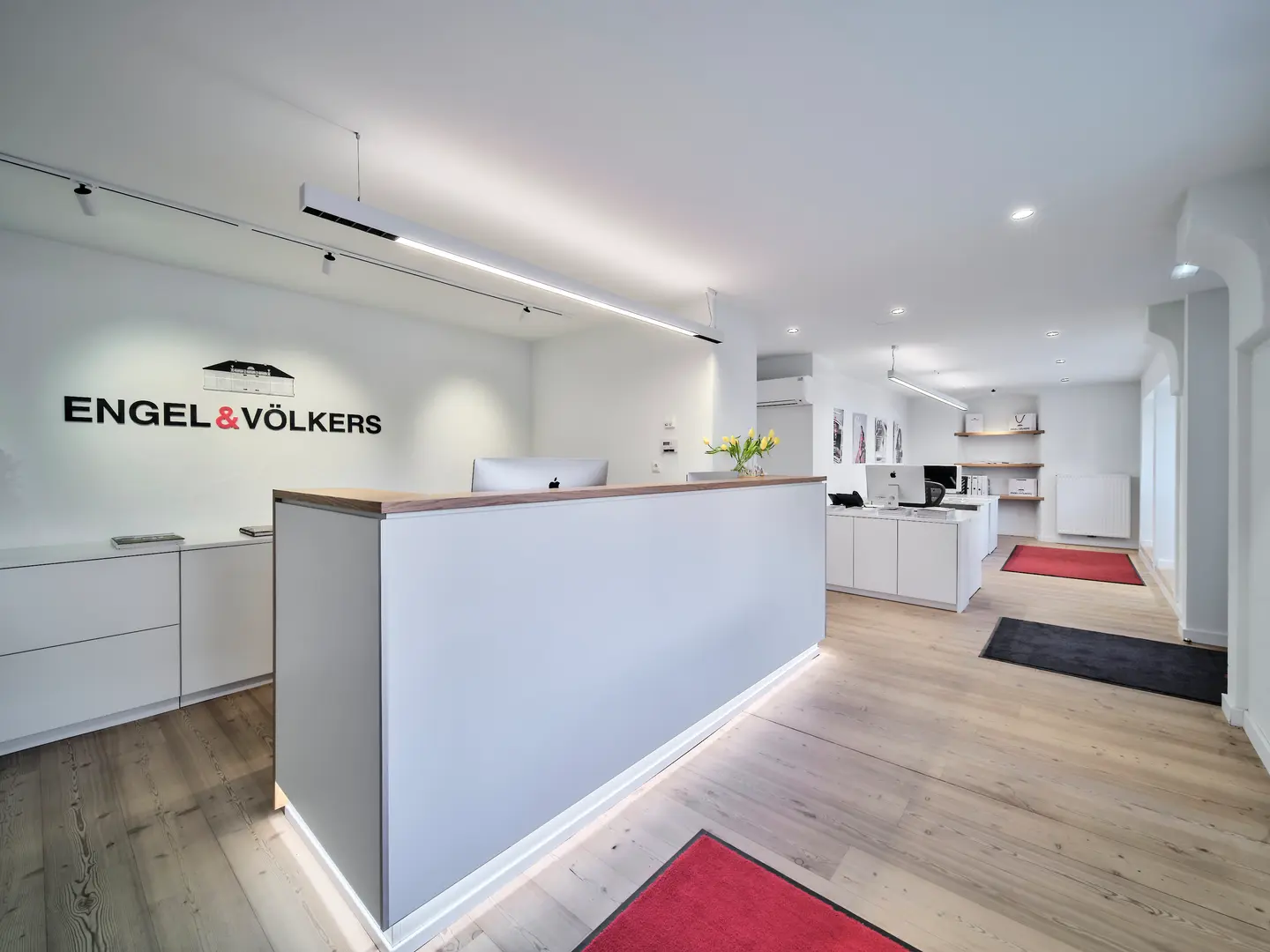 Bright real estate office interior with wood floors, white walls, and a reception desk with the Engel & Völkers logo.