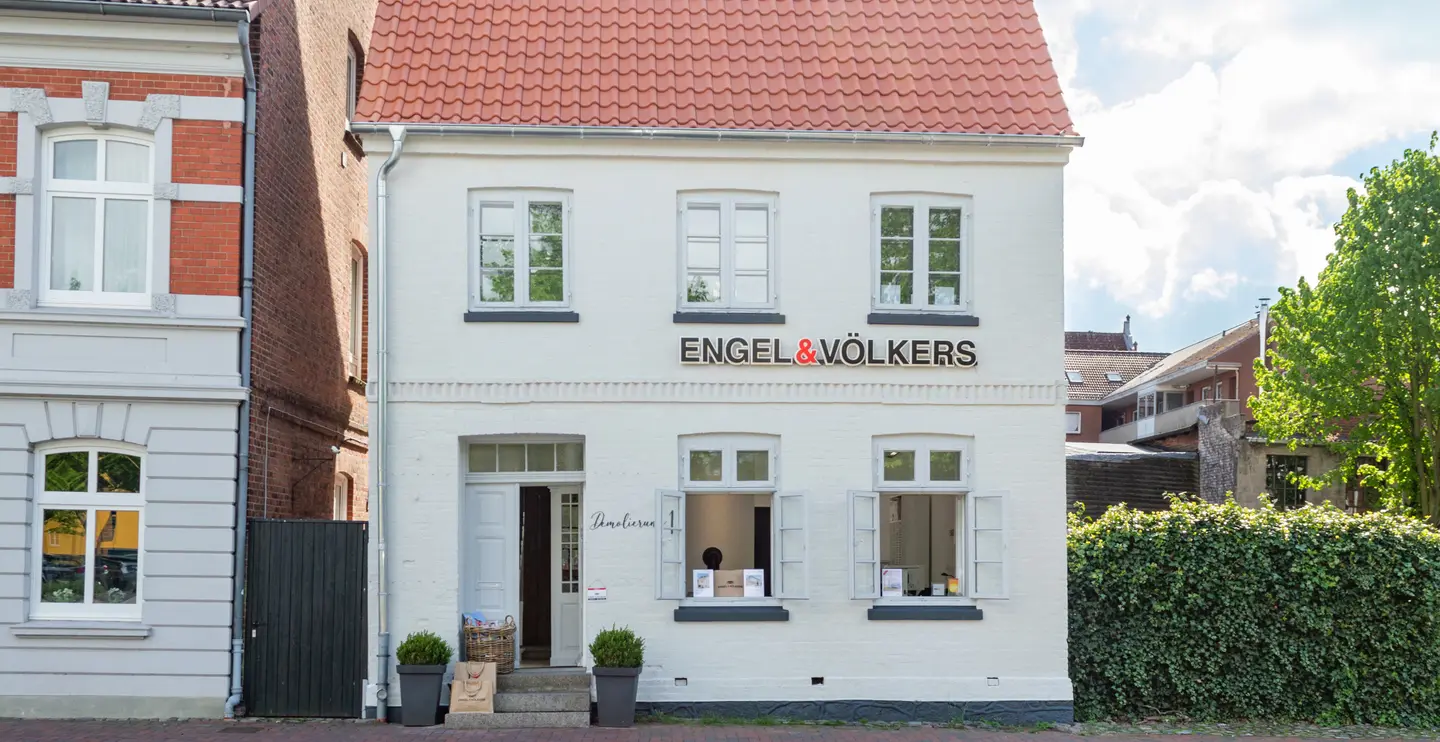Engel & Völkers real estate office. White building with red tile roof, open door, and window displays.