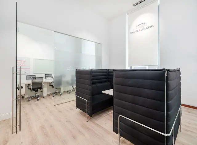 Interni dell'ufficio Engel & Völkers con cabine imbottite nere, sala conferenze con pareti in vetro e pavimenti in legno chiaro.