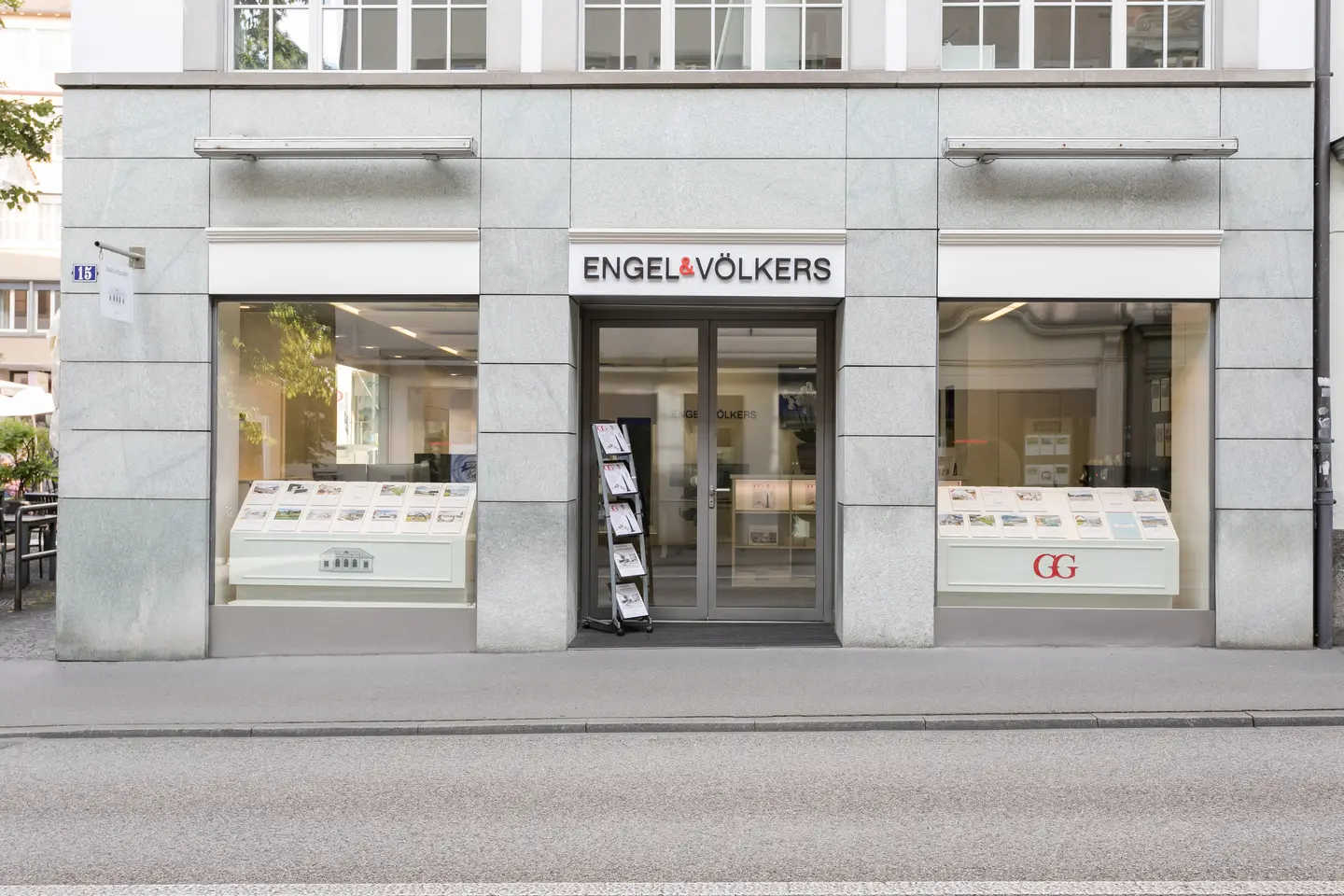 L'ufficio immobiliare Engel & Völkers con ampie vetrine che espongono annunci immobiliari e un espositore di brochure all'ingresso.