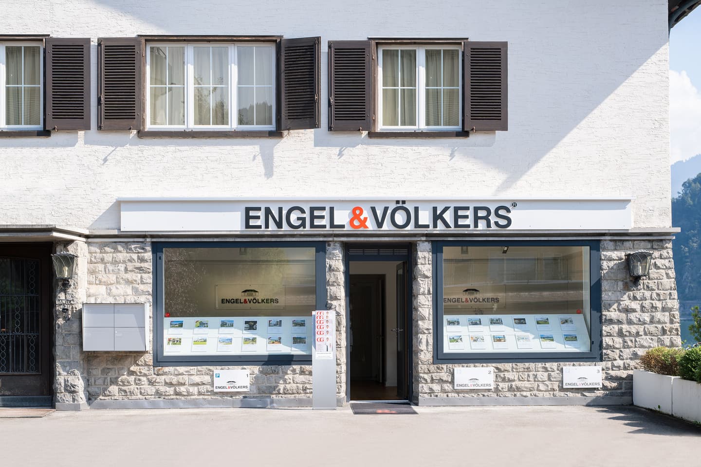 Engel & Völkers real estate office with white textured walls, brown shutters, and property listings in the window.