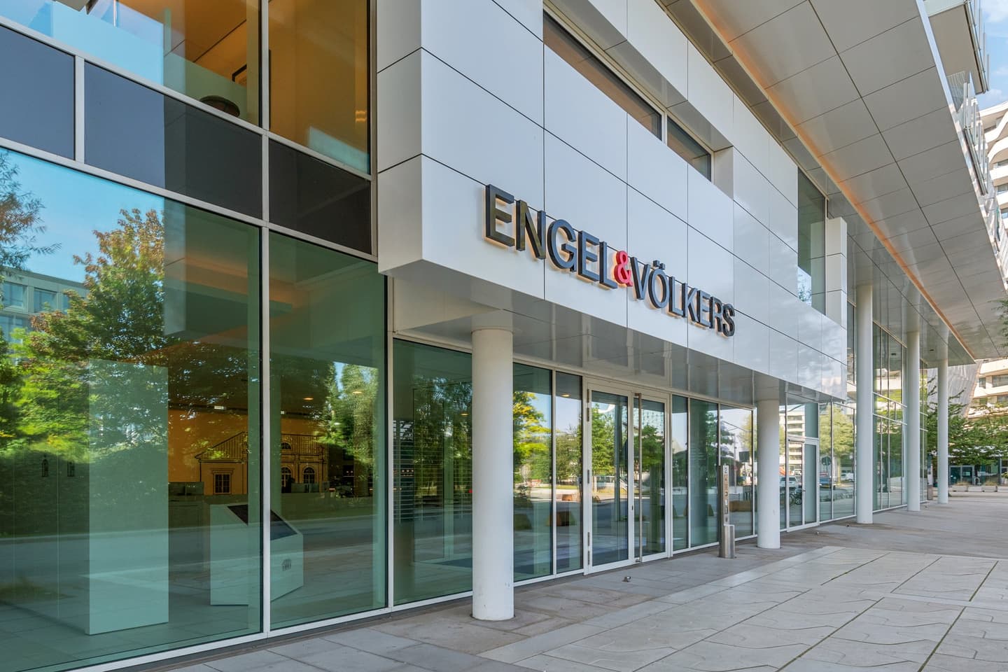 Exterior of Engel & Völkers office building with glass doors and windows. The company logo is displayed in gold lettering.