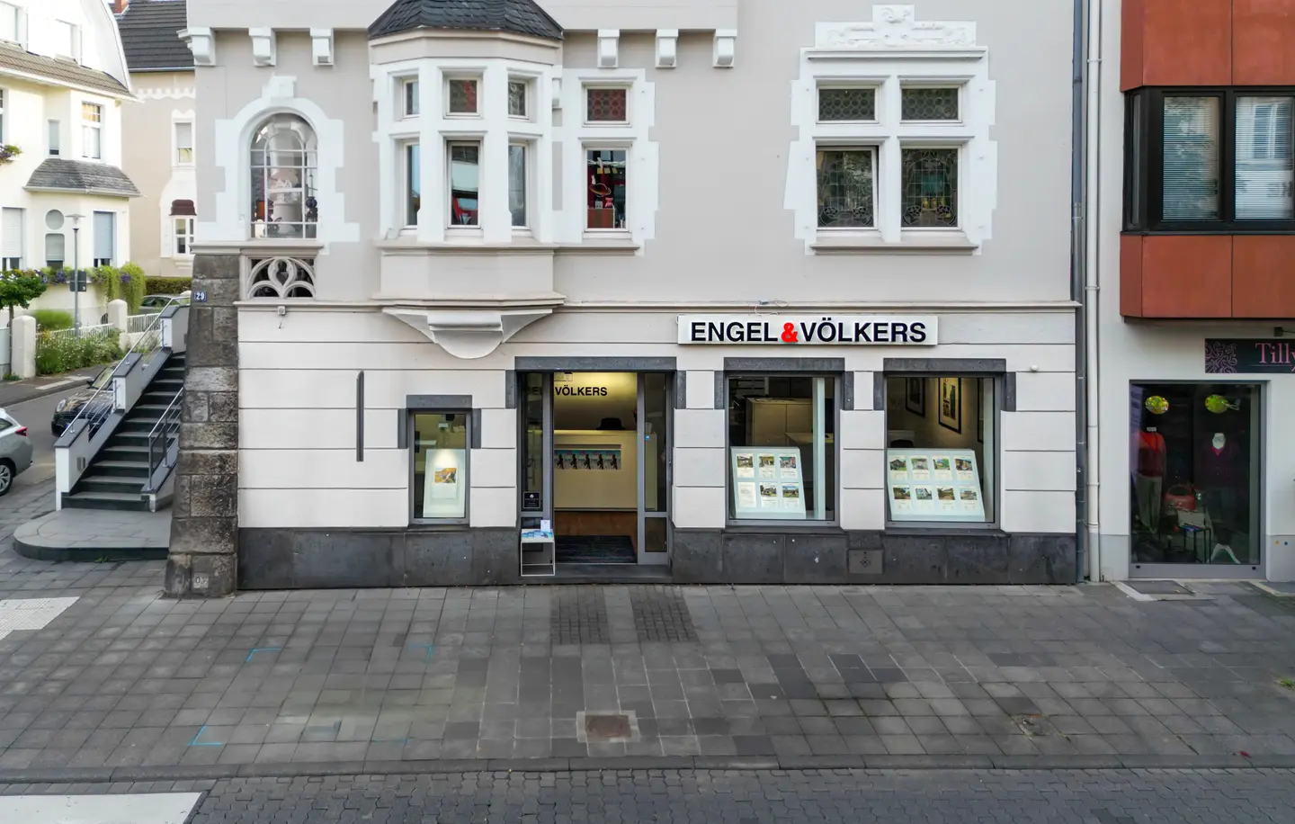 Engel & Völkers real estate office with large windows displaying property listings. The building is light gray with white trim.