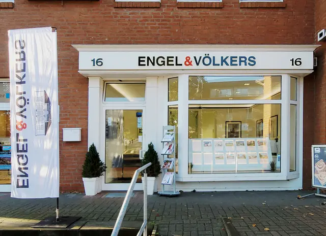 Engel & Völkers real estate office with a brick facade. A white flag with the company logo is on the left. The address "16" is above the entrance.