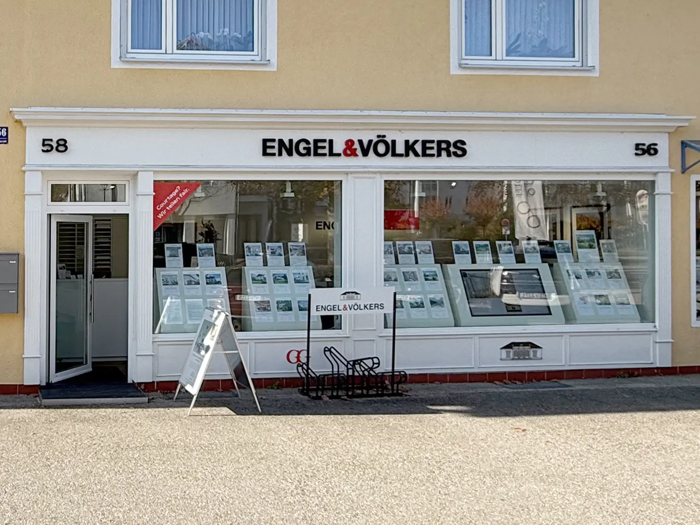 Engel & Völkers real estate office with property listings displayed in the window. An open door is on the left.