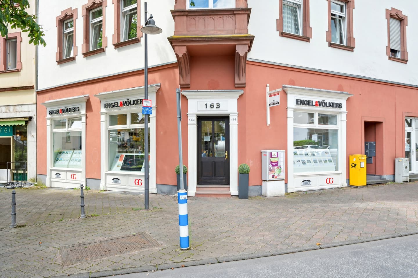 Engel & Völkers Immobilienbüro mit zwei weiß umrahmten Fenstern, in denen Immobilienangebote in einem pfirsichfarbenen Gebäude ausgestellt sind.