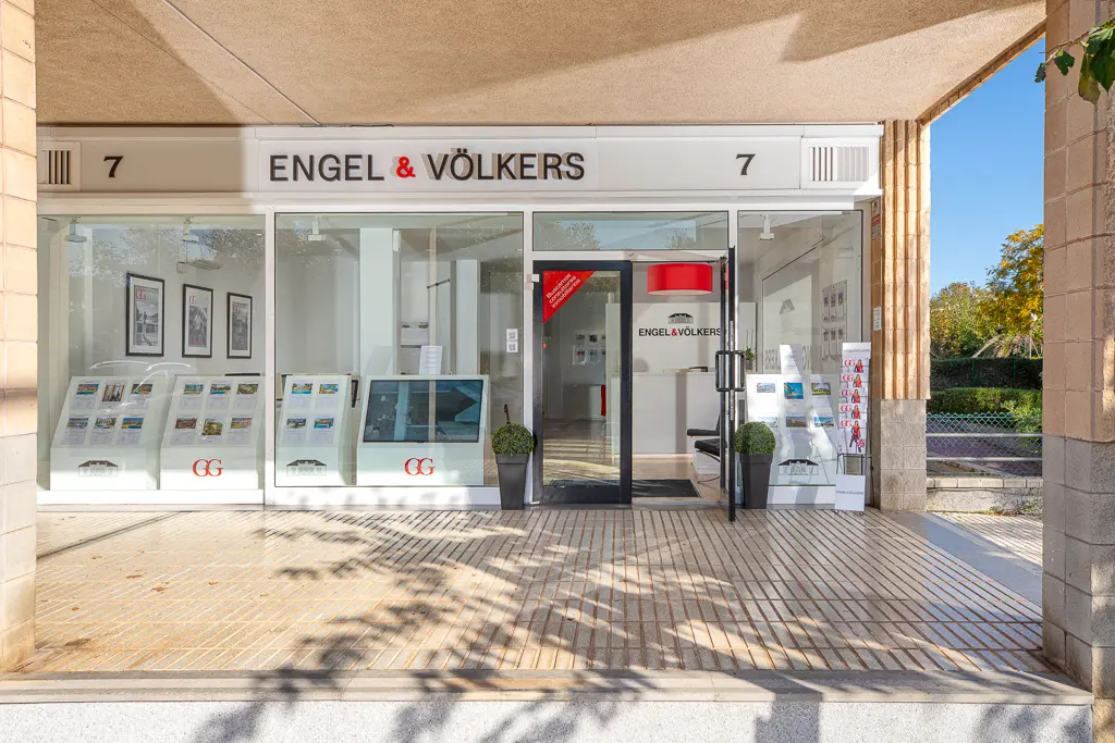 Das Engel & Völkers Immobilienbüro hat eine Glasfassade, an der Immobilienangebote ausgestellt sind. Die Tür ist offen und gibt den Blick auf ein modernes Interieur frei.
