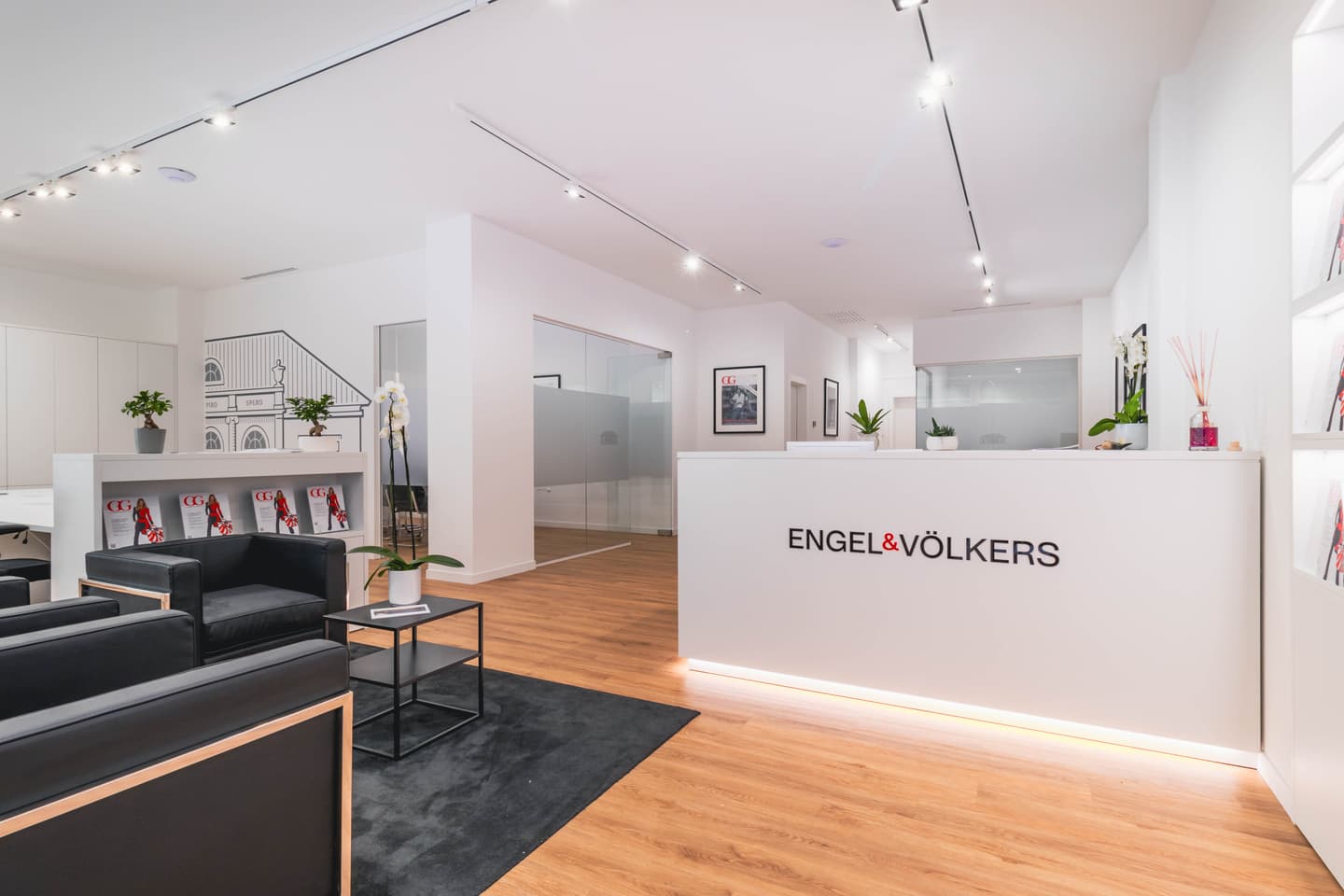 Engel & Völkers real estate office lobby with a white reception desk, black chairs, and wood floors.