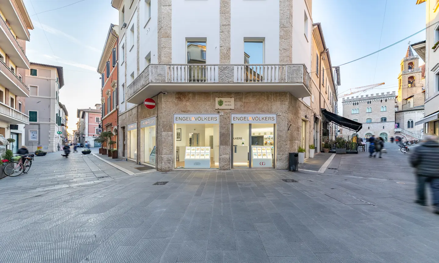 Engel & Völkers Immobilienbüro in einer europäischen Stadtstraße. Steingebäude mit großen Fenstern und Menschen, die vorbeigehen.