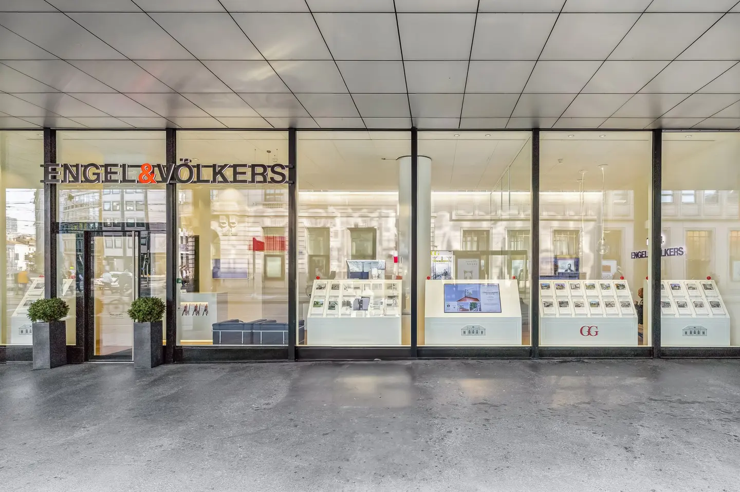 La devanture du bureau immobilier Engel & Völkers, avec ses vitrines en verre présentant des annonces immobilières et un plafond en tuiles grises.