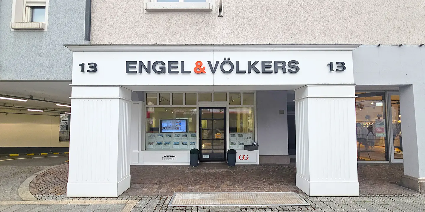 Engel & Völkers real estate office entrance with white pillars and the number 13 on top. A TV screen is visible inside.