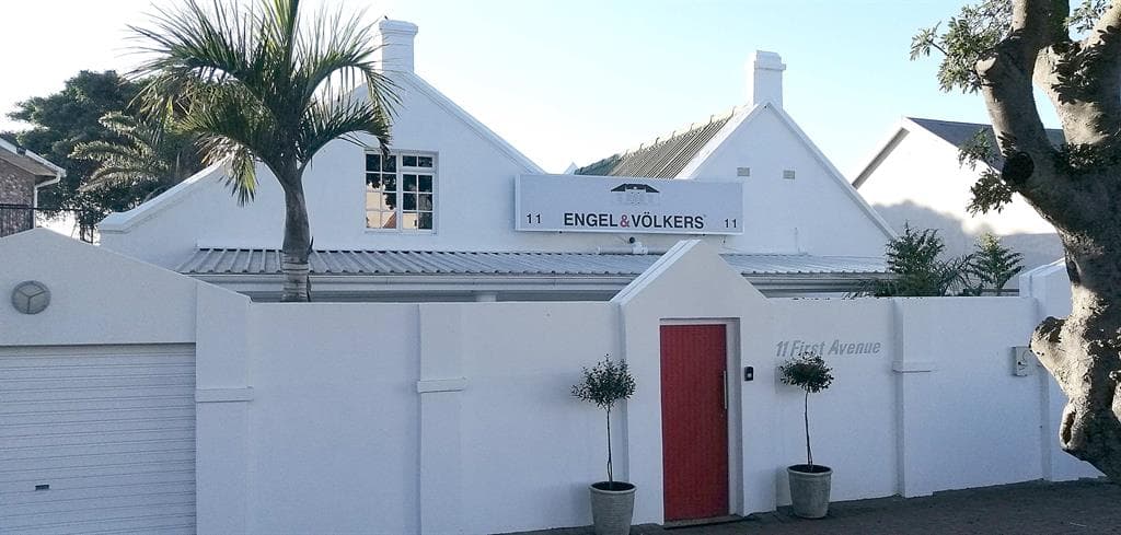 Engel & Völkers real estate office with white walls, a red door, and a palm tree in front.
